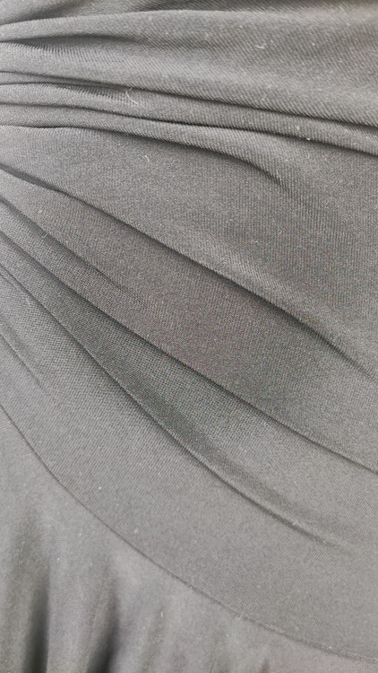 پیراهن زنانه وارداتی استوک مشکی بنددار، یقه هفت، فرم آزاد با پاییندوزی نامتقارن، قد حدود ۹۵ سانتیمتر، مناسب استایل مهمانی و شب، عکاسیشده روی تن با پسزمینه ساده روشن.