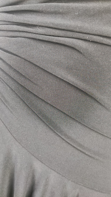 پیراهن زنانه وارداتی استوک مشکی بنددار، یقه هفت، فرم آزاد با پاییندوزی نامتقارن، قد حدود ۹۵ سانتیمتر، مناسب استایل مهمانی و شب، عکاسیشده روی تن با پسزمینه ساده روشن.