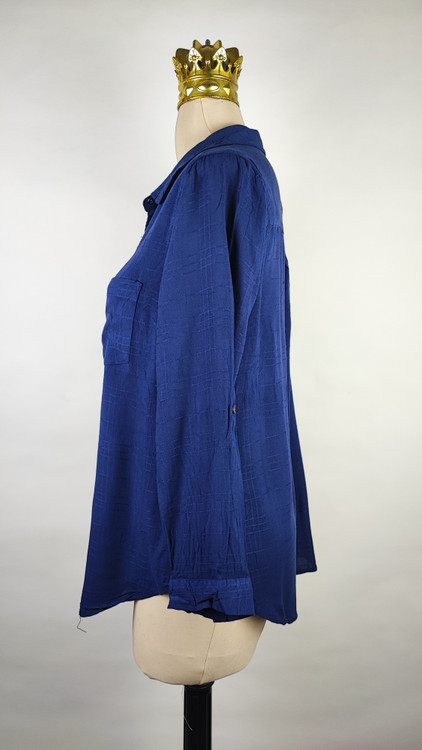 شومیز زنانه وارداتی استوک به رنگ آبی، مدل ساده و آزاد با یقه هفت و آستین بلند، مناسب سایز ۴۲–۴۴، عرض سینه ۵۵ و قد ۷۴ سانتیمتر، دارای ایراد، عکاسی روی تن با شلوار مشکی و پسزمینه روشن.