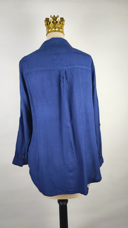 شومیز زنانه وارداتی استوک به رنگ آبی، مدل ساده و آزاد با یقه هفت و آستین بلند، مناسب سایز ۴۲–۴۴، عرض سینه ۵۵ و قد ۷۴ سانتیمتر، دارای ایراد، عکاسی روی تن با شلوار مشکی و پسزمینه روشن.