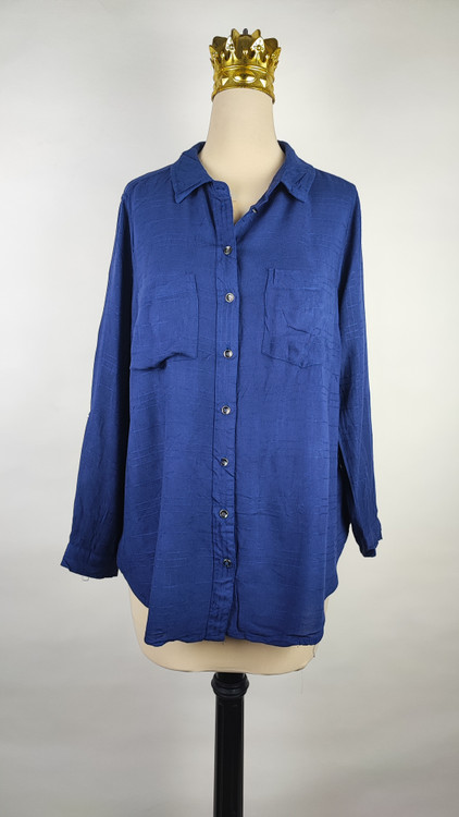 شومیز زنانه وارداتی استوک به رنگ آبی، مدل ساده و آزاد با یقه هفت و آستین بلند، مناسب سایز ۴۲–۴۴، عرض سینه ۵۵ و قد ۷۴ سانتیمتر، دارای ایراد، عکاسی روی تن با شلوار مشکی و پسزمینه روشن.