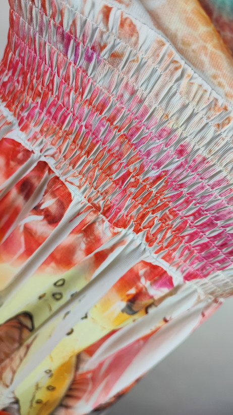 پیراهن زنانه وارداتی استوک با پارچه خنک و طرح گلدار رنگارنگ در تنالیته صورتی، نارنجی و کرم. مدل بندی و بدون آستین، مناسب سایز ۴۰ تا ۴۲ با عرض سینه ۵۰ و قد لباس ۹۵ سانتیمتر. تصویربرداری روی تن با پسزمینه روشن.